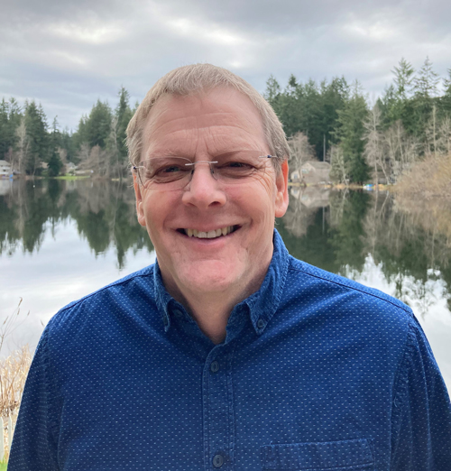 Man with glasses standing on lake edge smiling