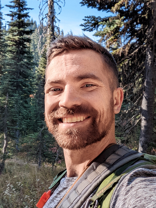 Bearded man standing in trees smiling