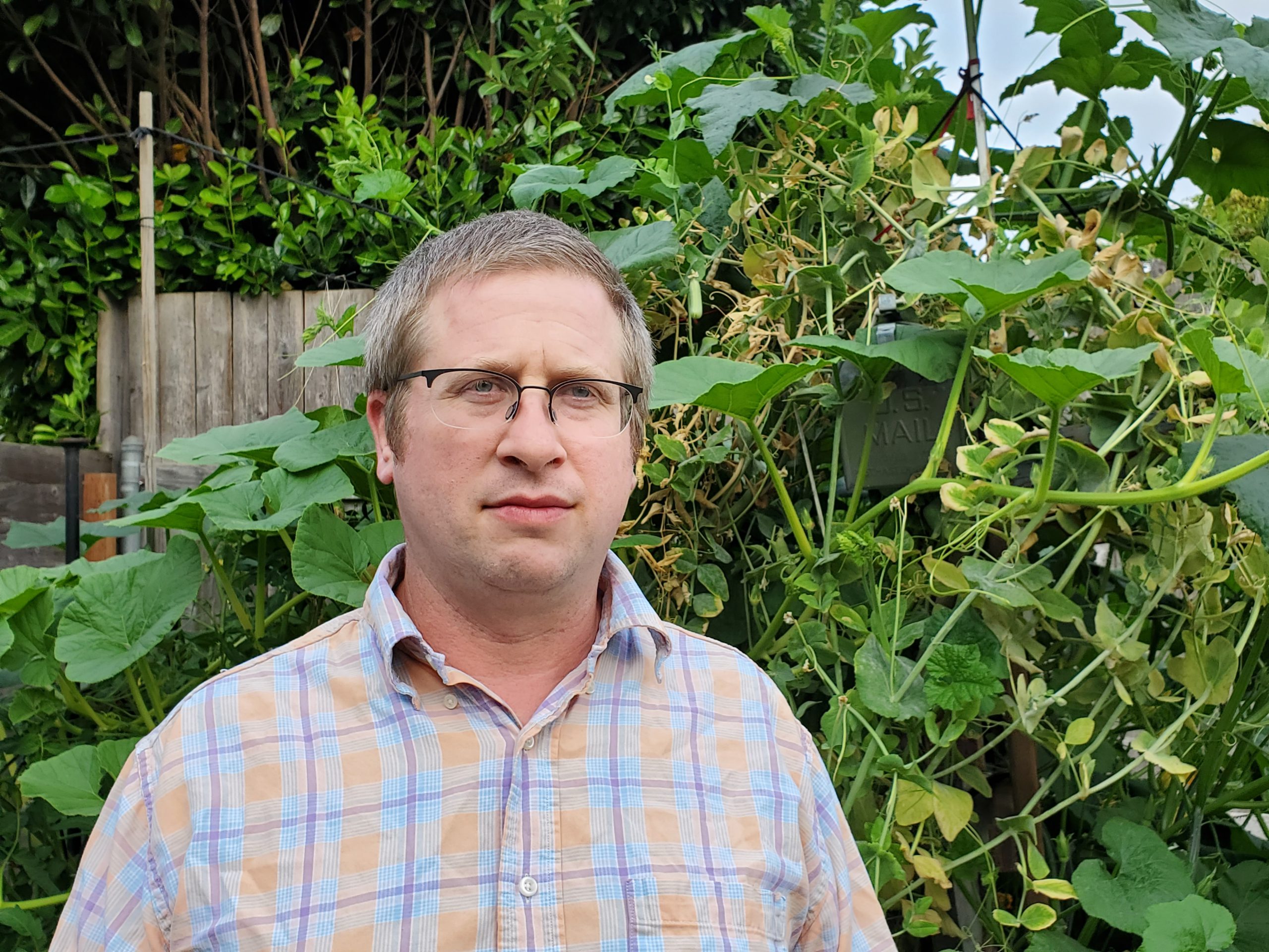 Man with glasses standing in front of a bush