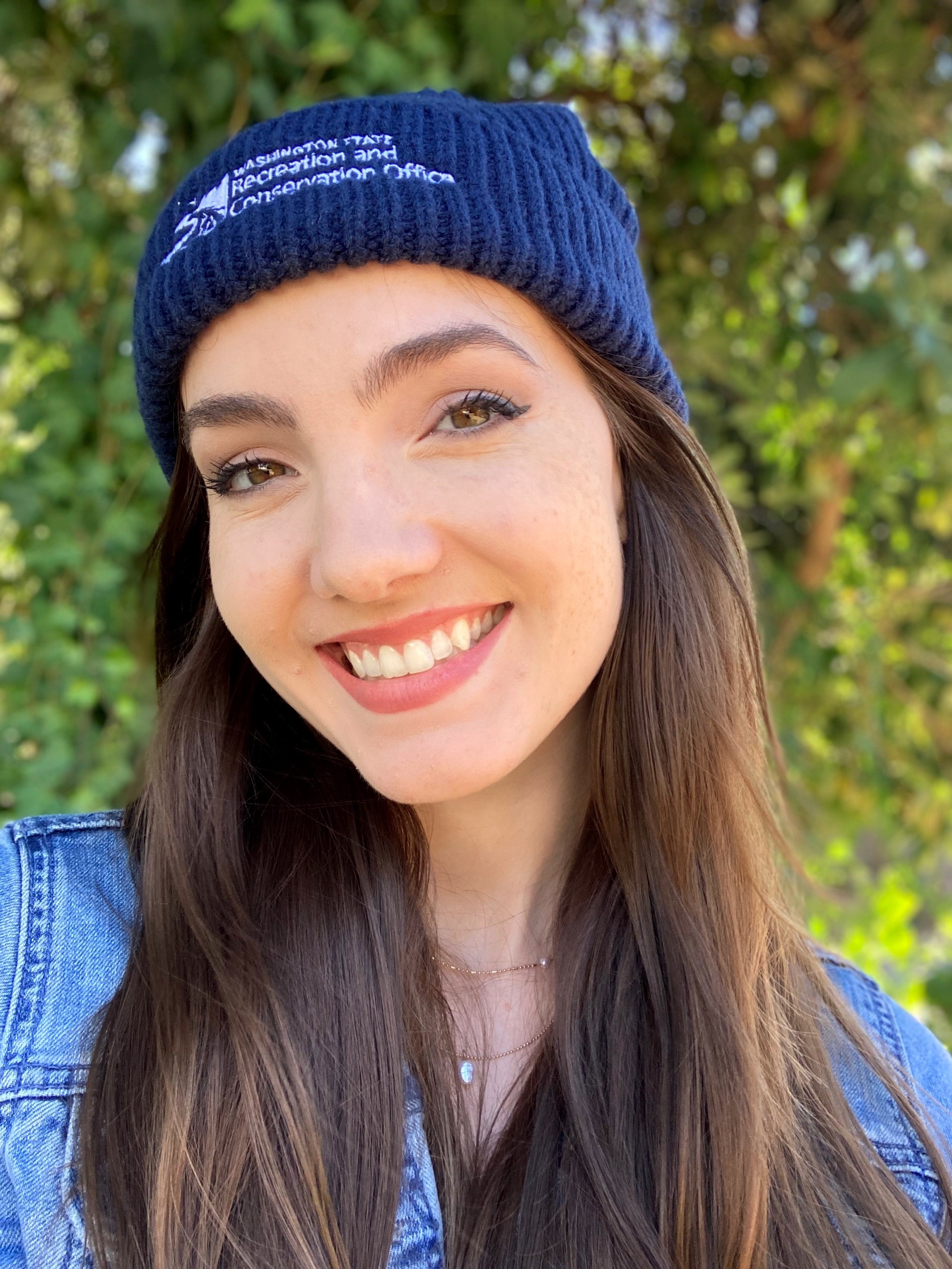 Woman wearing a blue beanie standing in front of a green bush