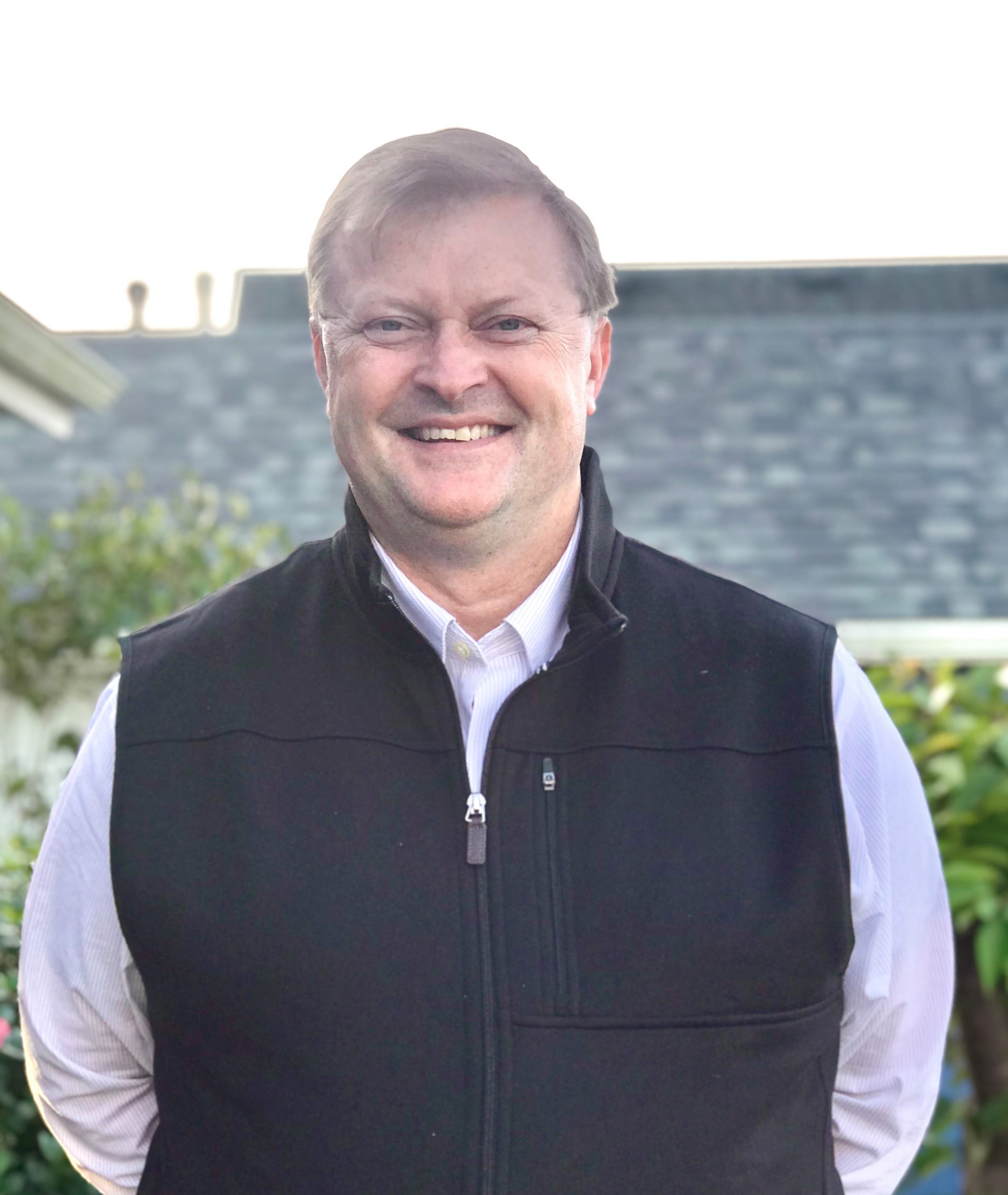 Man wearing a vest standing in front of a house.
