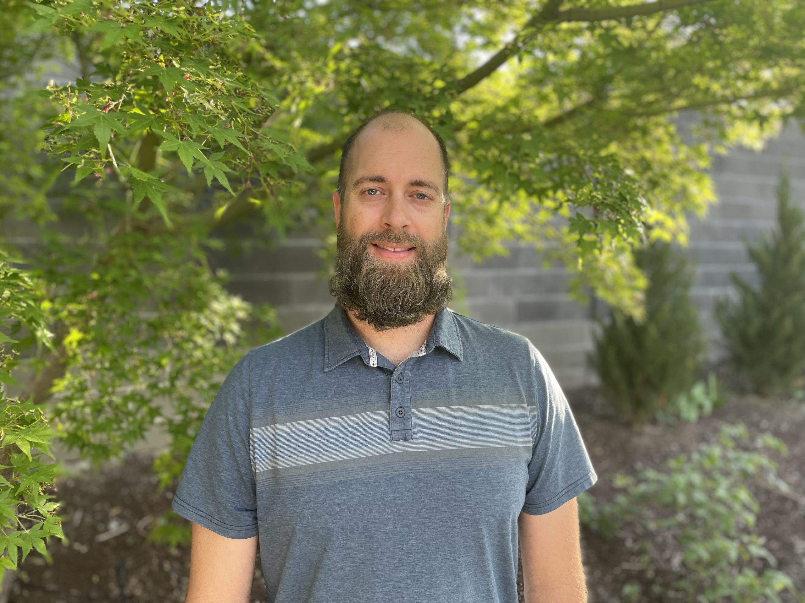 Bearded man standing in front of a tree.