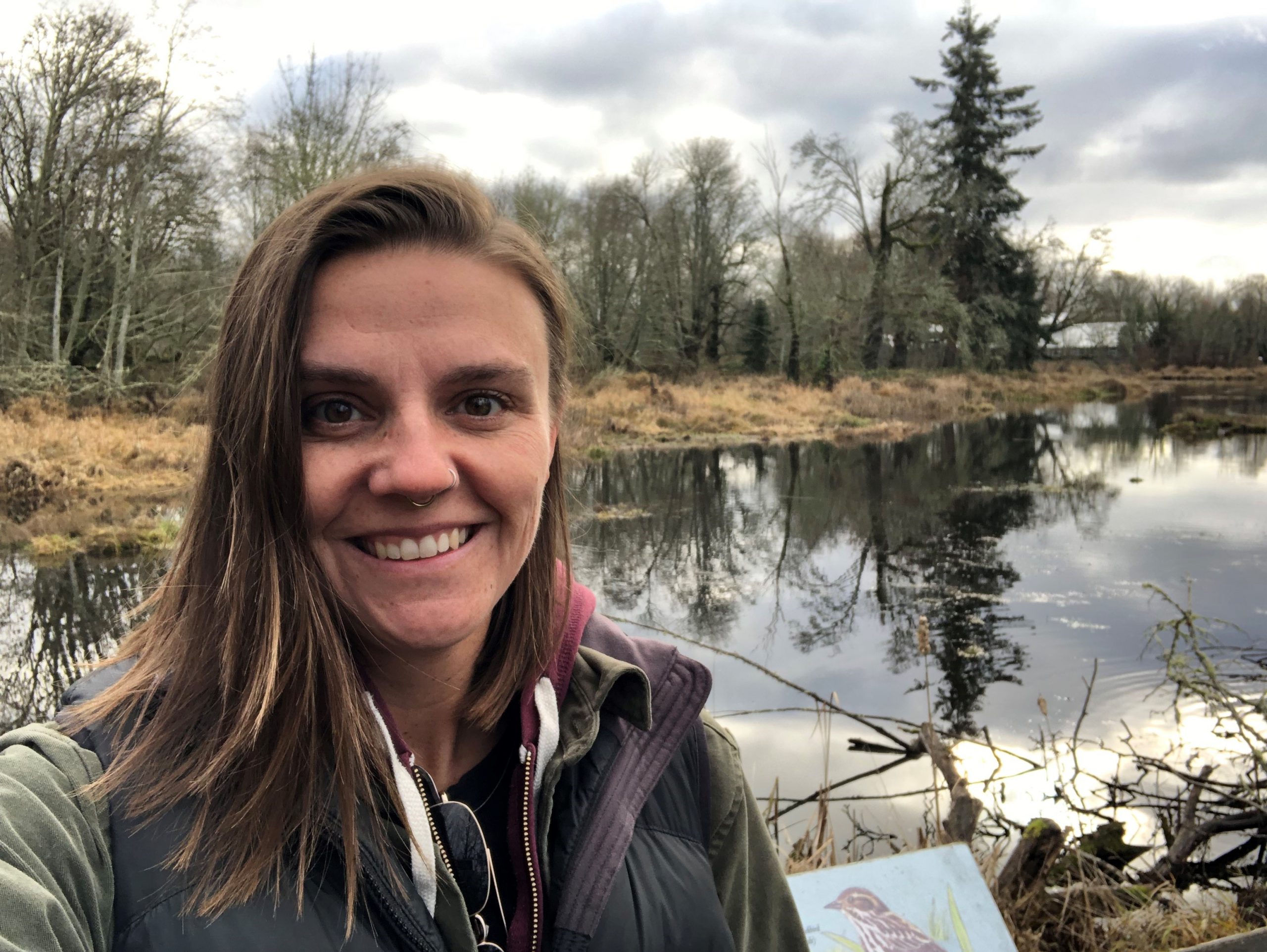 Blond woman posing for a selfie while standing in front of a pond.