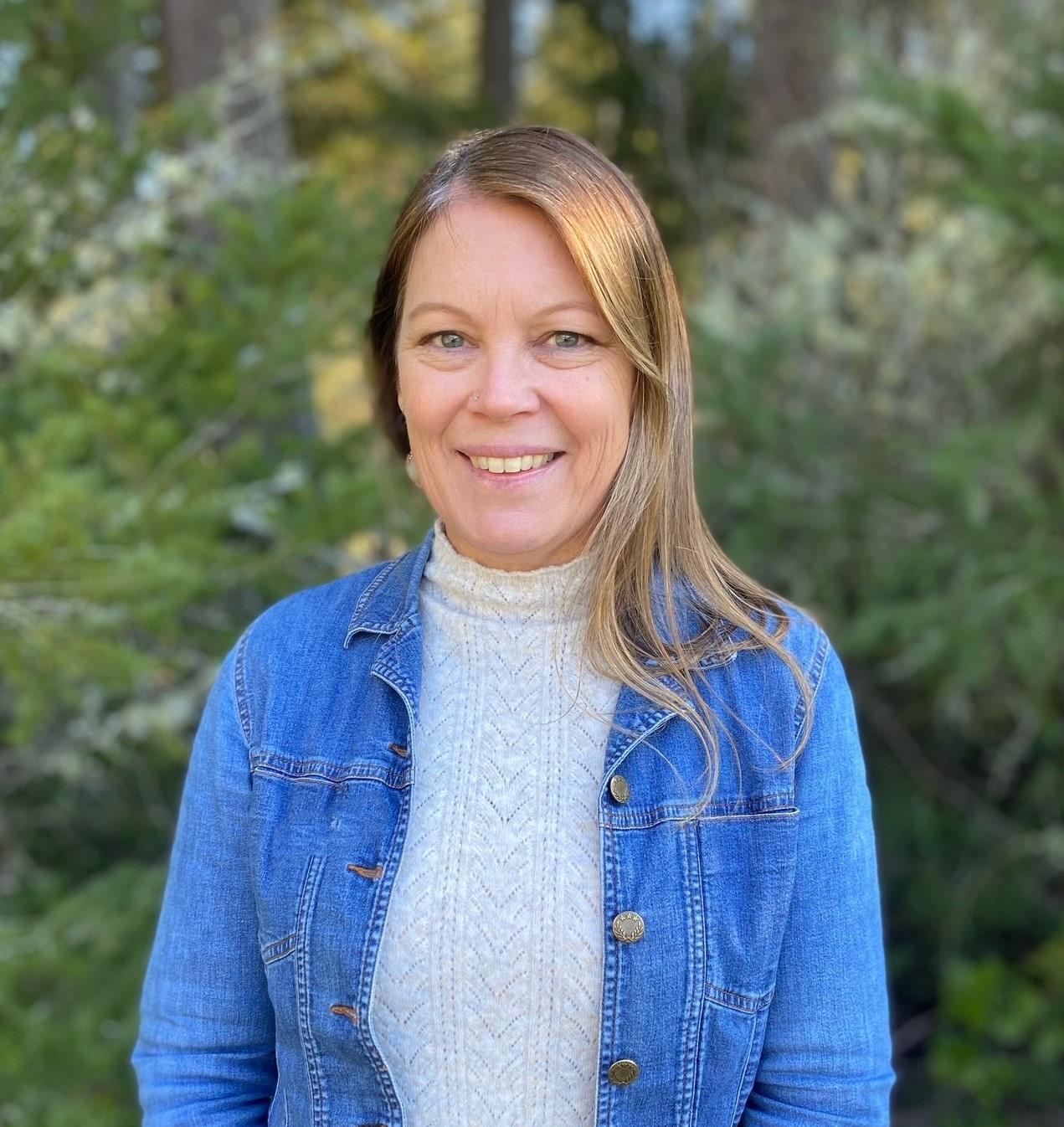 Woman with blond hair wearing a gray high-neck sweater and a jean jacket