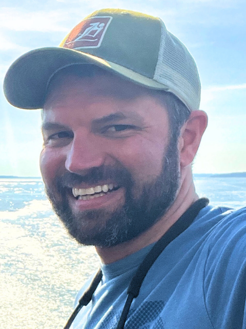 Bearded man wearing a baseball cap and a blue shirt while smiling